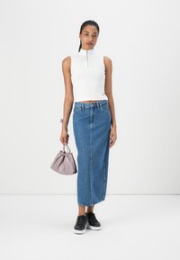 Vit ärmlös cropped topp med dragkedja, hög midja blå denim maxikjol, svarta sneakers och en liten lavendelfärgad dragsko-väska.
