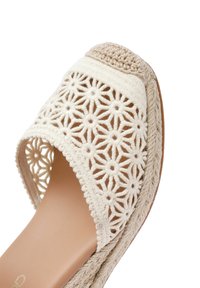 Sandalia de punta abierta con un upper de croché en color crema que presenta patrones florales, una suela intermedia de cuerda trenzada y una plantilla suave en color beige.