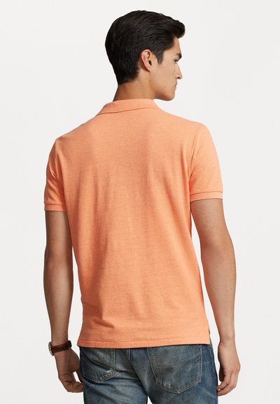 Tricou polo cu mânecă scurtă din material portocalie aprins, având un guler clasic și un țesătură texturată, asociat cu blugi albaștri uzați.