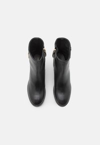 Botas de tobillo de cuero negro con una textura suave, que presentan cremalleras doradas a los lados y un diseño de punta redondeada.