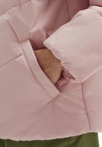 Jasnoróżowa kurtka puchowa z boczną kieszenią i elastycznymi mankietami. Materiał ma gładką, błyszczącą teksturę.