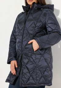 Marine blauwe gewatteerde pufferjas met capuchon, voorzien van ritszakken, een ritssluiting aan de voorkant en een diagonaal patroon in een glanzende textuur.