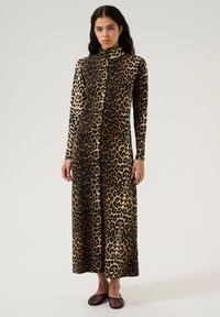 Vestido largo de estampado de leopardo con cuello alto, hecho de tela suave, que presenta patrones en contraste de marrón y negro, combinado con bailarinas de malla negras.