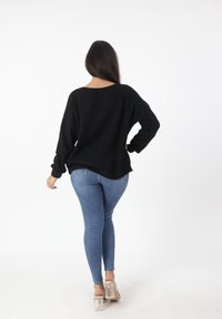 Czarny dzianinowy sweter o luźnym kroju, z szerokim dekoltem i długimi rękawami, w połączeniu z niebieskimi jeansami skinny i przezroczystymi sandałami na obcasie.