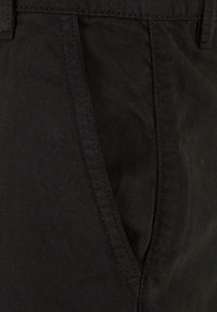 Pantaloni negri din bumbac, cu un material texturat, buzunare laterale și detalii de cusătură discrete de-a lungul cusăturilor.