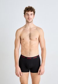 Black boxer shorts with a red "HUGO" waistband, fitted design, made from stretchable fabric, featuring a smooth texture and minimalist style.
