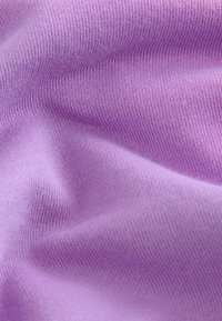 Gros plan d’un tissu lavande doux et texturé avec un motif tricoté visible et des plis doux créant des variations de lumière et d’ombre.