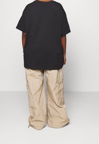 Lös passform svart bomullströja med korta ärmar, i kombination med beige cargobyxor med en skrynklig textur och sidofickor.