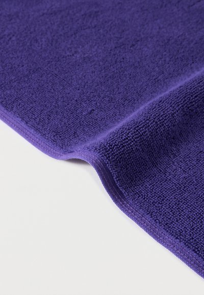 Κοντινή λήψη διπλωμένου μωβ μικροϊνικού πανιού καθαρισμού που δείχνει απαλό υφασμάτινο υφή και ραμμένα άκρα σε λευκή επιφάνεια.