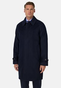 Mornarsko modra volnena jakna s prahom z notch ovratnikom, gumbnimi detajli in dvema stranskima žepoma. Rob sega pod kolena za uglajen videz.