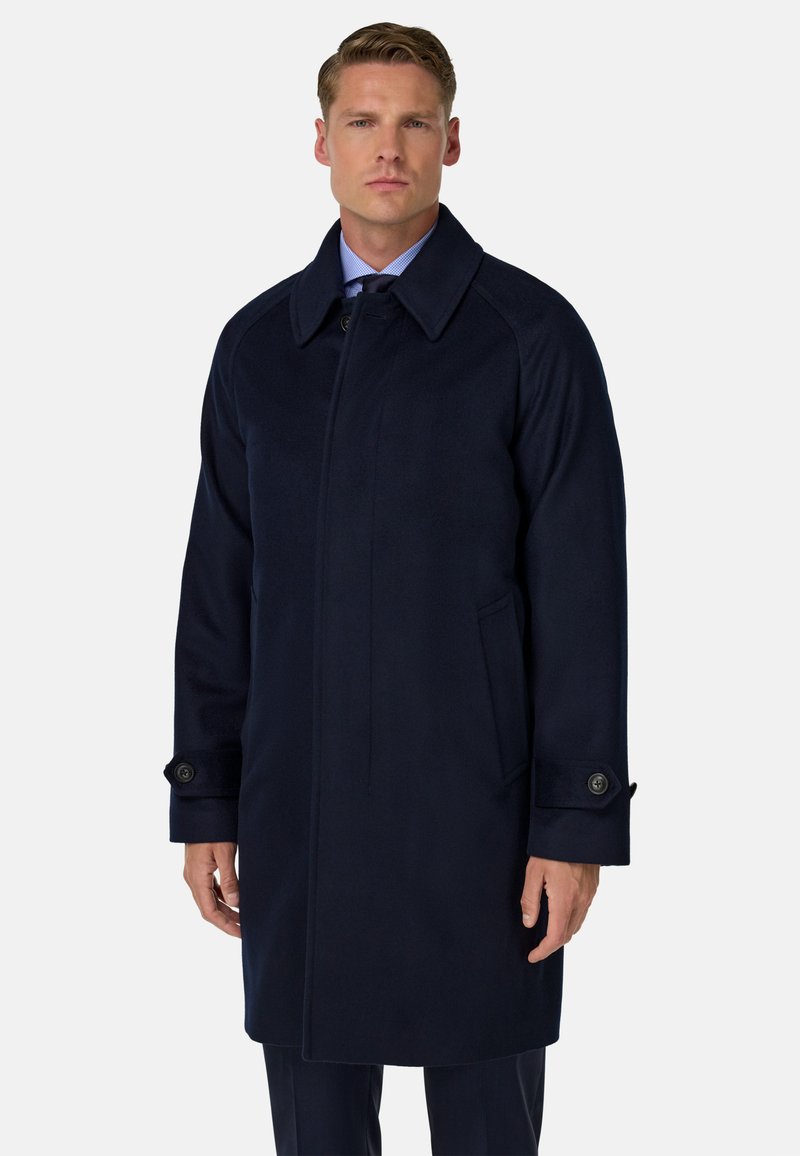 Mornarsko modra volnena jakna s prahom z notch ovratnikom, gumbnimi detajli in dvema stranskima žepoma. Rob sega pod kolena za uglajen videz.