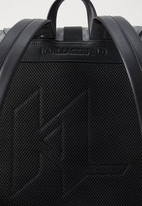 Un sac à dos noir avec un panneau en maille et un logo texturé, des accents en cuir élégants et des bretelles ajustables. Design léger avec une esthétique moderne.