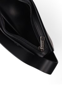 Zwarte leren schoudertas met een ritssluiting, een gladde textuur en een sleek ontwerp. Inclusief metalen hardware met een merklogo-detail.