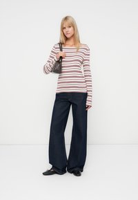 Blusa de manga longa às riscas em creme e bordô, combinada com jeans de perna larga em denim escuro. A modelo segura uma pequena mala preta e usa sapatos pretos.