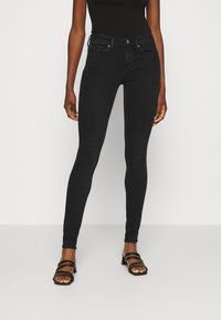 Jeans negros ajustados con una cintura alta, presillas para cinturón y bolsillos frontales. Presenta una textura de mezclilla elástica suave y detalles de costura sutiles.