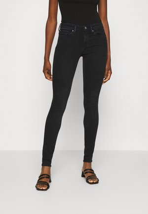Jeans negros ajustados con una cintura alta, presillas para cinturón y bolsillos frontales. Presenta una textura de mezclilla elástica suave y detalles de costura sutiles.