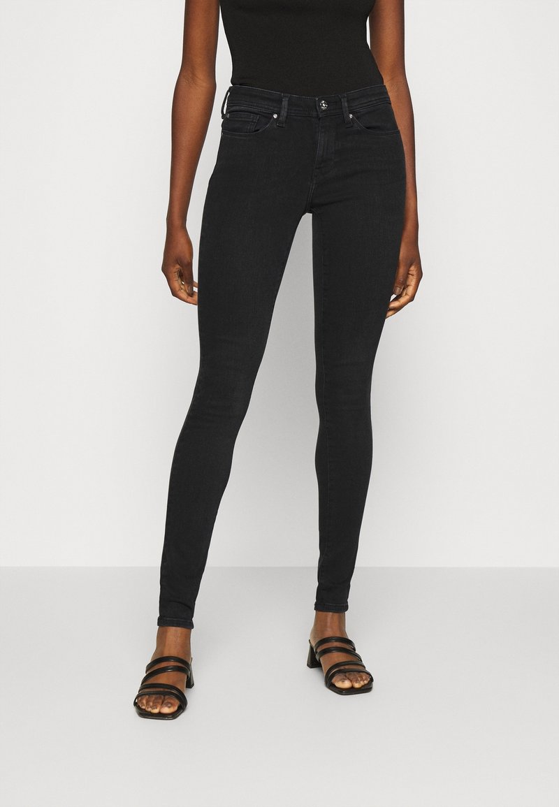 Jeans negros ajustados con una cintura alta, presillas para cinturón y bolsillos frontales. Presenta una textura de mezclilla elástica suave y detalles de costura sutiles.