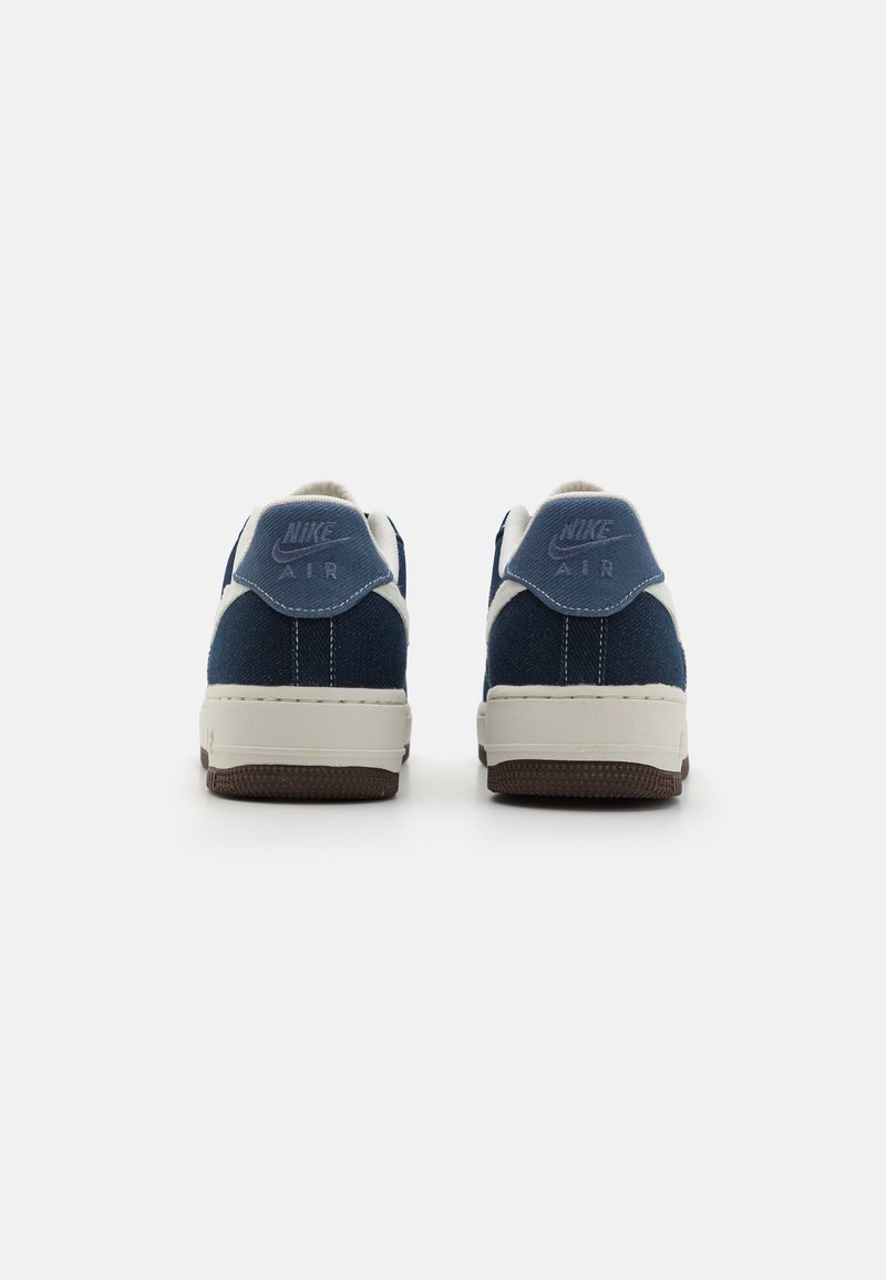 Blaue Denim-Sneaker mit weißen Akzenten und hellbraunen Gummisohlen. Verfügt über eine Nike-Branding an der Ferse und eine strukturierte Oberfläche. Niedrigschuh-Design.