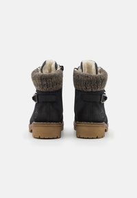 Bottines en cuir noir avec un col tricoté marron et gris, mettant en avant une boucle décorative, une doublure en fausse fourrure et une semelle en caoutchouc légère.