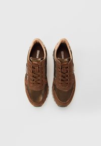 Une paire de baskets en cuir et en suède marron avec des lacets, des semelles intérieures de marque et des cols rembourrés, présentée vue de dessus sur un fond blanc.