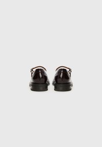 Burgundy leather shoes with a glossy finish, featuring a single strap across the ankle, set on a black rubber sole.