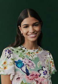 Blusa con motivo floreale e maniche a sbuffo in colori vivaci, che presenta tonalità di verde, rosa, blu e viola su tessuto morbido.