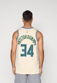 Krémový basketbalový dres má modro-zelený pruhovaný výstrih. Na chrbte je vytlačené "ANTETOKOUNMPO" a "34" v zelenej farbe.