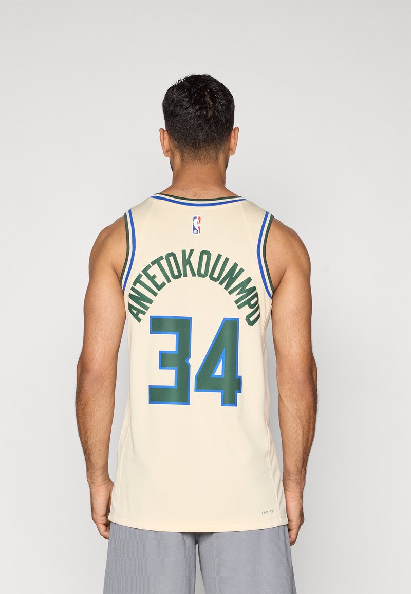 La camiseta de baloncesto de color crema presenta un cuello a rayas en azul y verde. "ANTETOKOUNMPO" y "34" están impresos en la parte trasera en color verde.