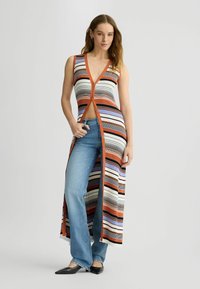 Gebreide, mouwloze jurk met een diepe V-hals, oranje rand en meerkleurige strepen. Voorzien van een sluiting met knopen aan de voorkant en een vlotte uitstraling. Gekoerst met jeans.