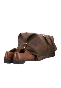Bolsa de viaje de cuero marrón con compartimento lateral parcialmente abierto, revelando un par de zapatos de vestir de cuero marrón almacenados en su interior.