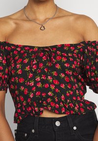 Czarna bluzka typu off-shoulder z krótkimi bufkowymi rękawami, zdobiona czerwonymi kwiatowymi wzorami, z wiązaniem na sznurki i falbaniastym dołem.