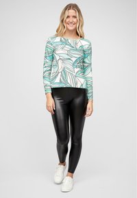 Haut à manches longues avec un motif de feuilles vertes et blanches, associé à des leggings noirs brillants et des baskets blanches ; tissu lisse et coupe ajustée.