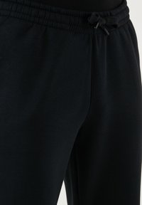 Schwarze Baumwoll-Jogginghosen mit einem elastischen Bund und einem Kordelzug. Glatte Textur und schmal zulaufendes Beindesign ohne Taschen.