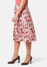 Plisségedeelte in het wit met een rood en roze bloemenpatroon. Elastische tailleband. Gestyled met bruine hoge hakken.