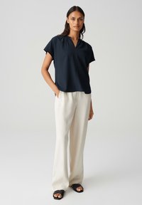 Top blu navy a maniche corte con scollo a V, abbinato a pantaloni a gamba larga crema e sandali neri. Tessuto liscio con una texture sottile.
