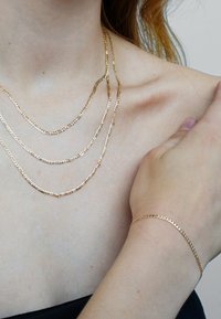 Gold-tone jewelry featuring three layered chain necklaces with rectangular links and a matching thin bracelet. Smooth texture with shiny finish.