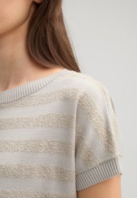 Lichtgrijze trui met horizontale beige strepen, gestructureerde stof, geribde kraag en korte mouwen. Zachte en casual uitstraling.