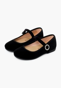 Zapatos Mary Jane de terciopelo negro con un acento plateado redondo en la correa, suela plana, textura suave y diseño de punta redondeada.
