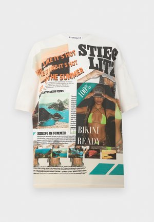 Woman wearing oversized graphic long-sleeve shirt with beach images and text, paired with a two-tone denim maxi skirt and black sunglasses.