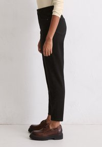 Czarne, wysokogatunkowe dżinsy z denimowy materiału, z prostą nogawką, bocznymi kieszeniami i subtelnym wykończeniem tylnych kieszeni, w połączeniu z ciemnobrązowymi butami.