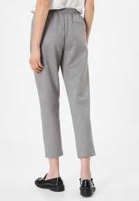 Pantalones de ante sintético grises con cintura elástica, pierna ajustada y un bolsillo trasero, combinados con zapatos negros sin cordones.