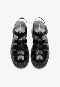 Black platform sandals featuring a woven strap design, adjustable ankle buckle, and textured sole for enhanced grip.
