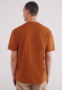 Korte mouwen, ronde hals t-shirt in roestoranje, gemaakt van lichtgewicht katoen, heeft een ontspannen pasvorm en een gladde textuur.