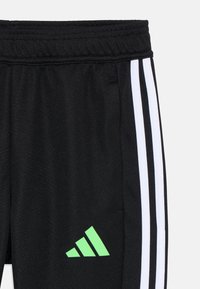 Zwarte sportbroek met witte strepen aan de zijkanten, voorzien van een groen Adidas-logo op het onderbeen en een elastische tailleband.