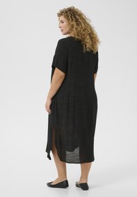 Robe noire, longue, amples avec des manches courtes. Tissu léger et transparent avec des fentes latérales allant jusqu'aux chevilles. Design simple.