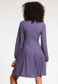 Långärmad, knälång klänning i lila tyg med ett ljusblått blommönster. Har en åtsittande midja och en utsvängd kjol. Slät textur.