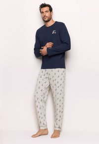 Navy long-sleeve top with small chest print, paired with light gray pajama pants featuring blue cartoon character patterns. Soft fabric.