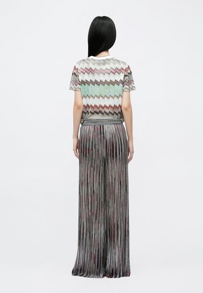 Csíkos kötött felső világos színű cikk-cakk mintával; bőszárú, pliszírozott nadrág sötét árnyalatú, függőleges csíkokkal és fémes részletekkel.