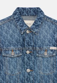 Chaqueta de denim con un patrón de monograma azul. Cierre de botones, dos bolsillos frontales y detalles de costura contrastantes. Etiqueta de Calvin Klein presente.