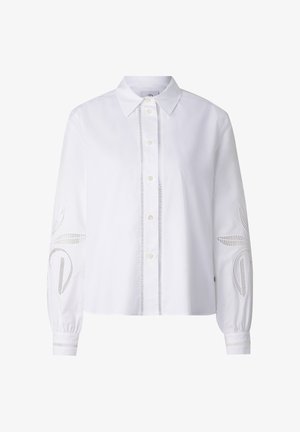 Hvid skjortebluse med knapper, spids krave, lange ærmer og dekorative udskæringsmønstre på ærmer og forstykke.